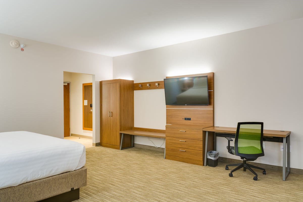 Una camera d'albergo con un letto, una scrivania in legno con un televisore e una sedia.