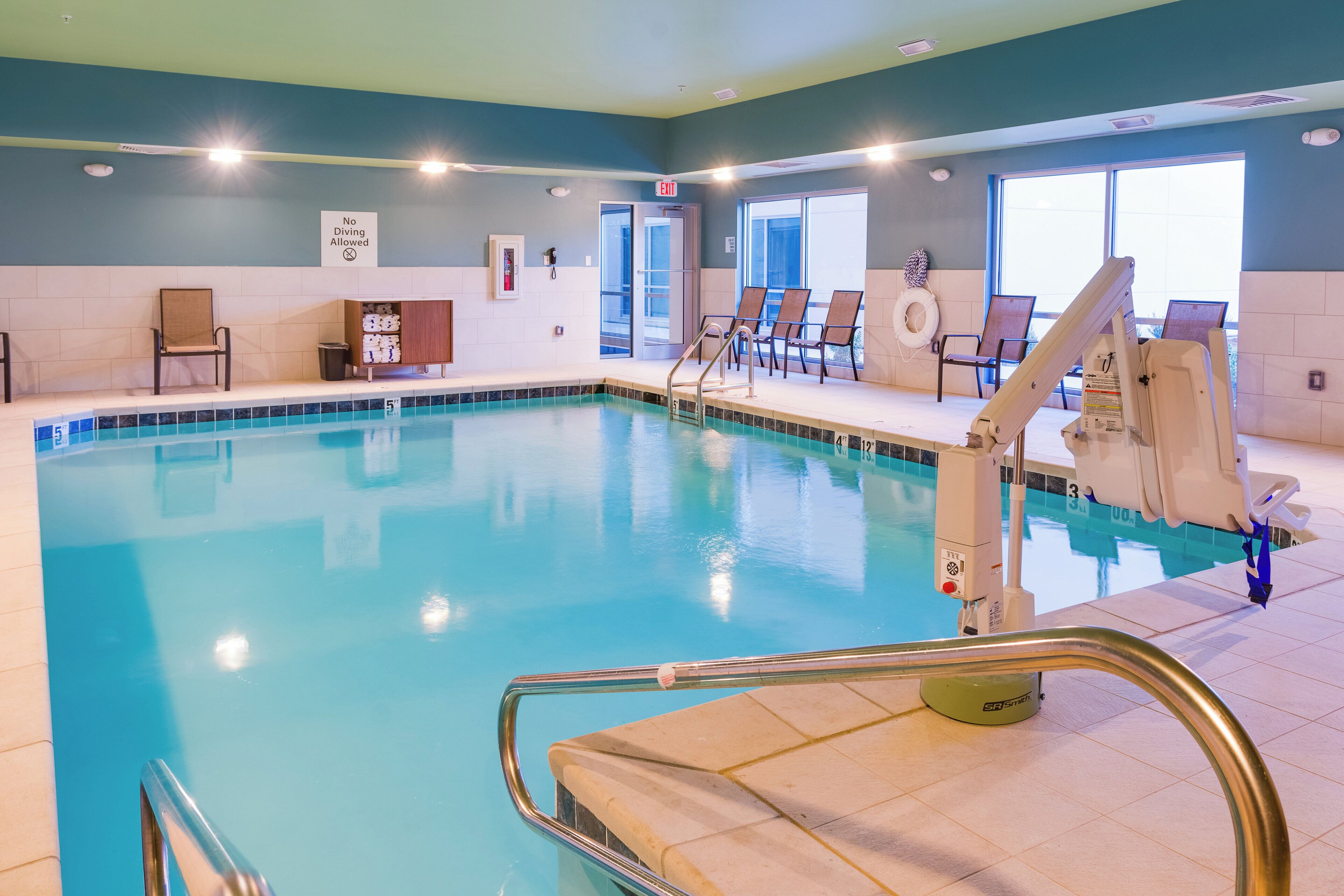 An indoor swimming pool with clear water, a lifeguard chair, and a pool ladder.
