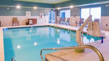 An indoor swimming pool with clear water, a lifeguard chair, and a pool ladder.