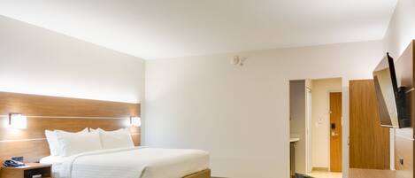 Une chambre d’hôtel comprenant un lit, une table de chevet, une télévision et une porte donnant accès à une salle de bain.