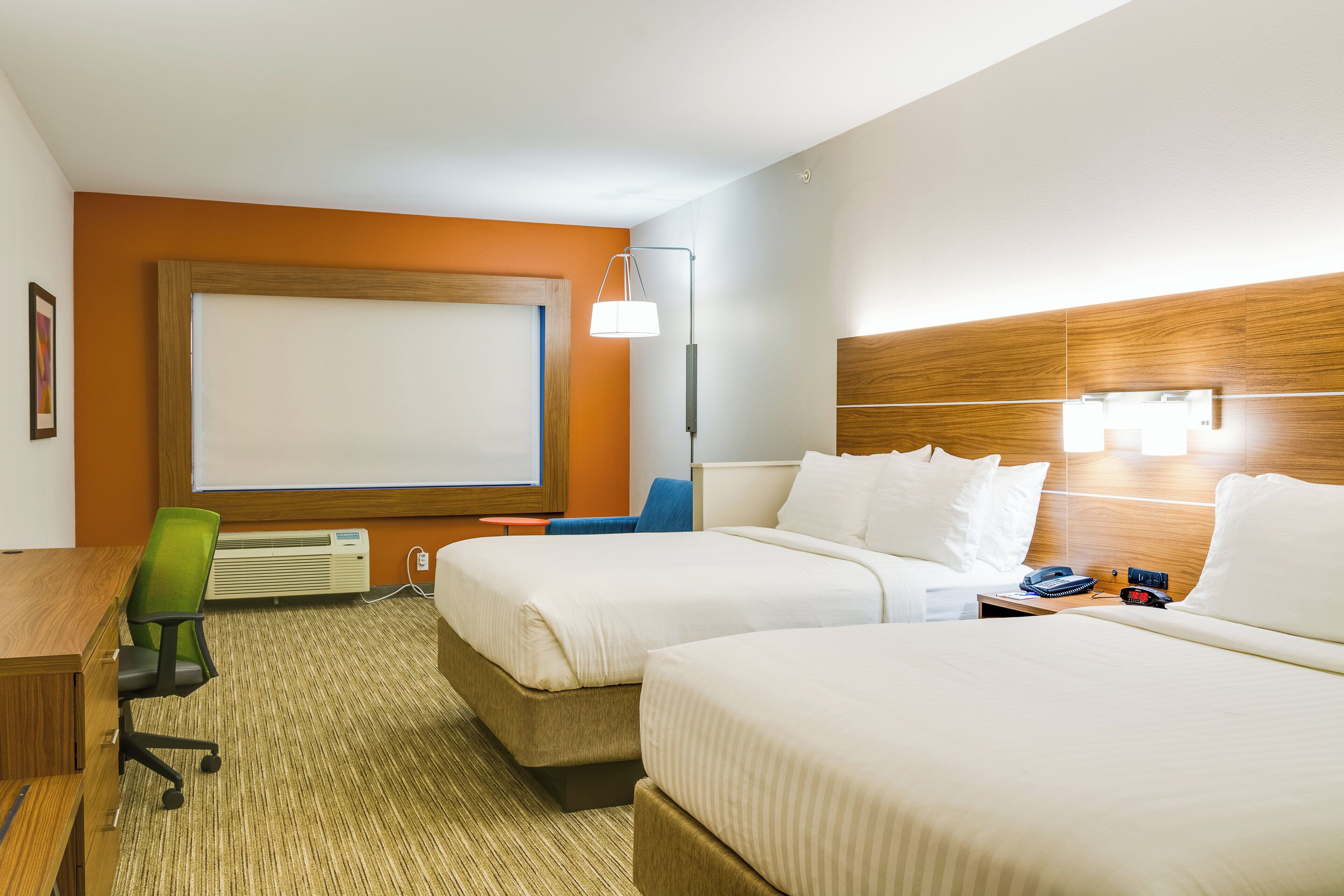 A hotel room with two beds, a desk, a chair, a lamp, and a large window.