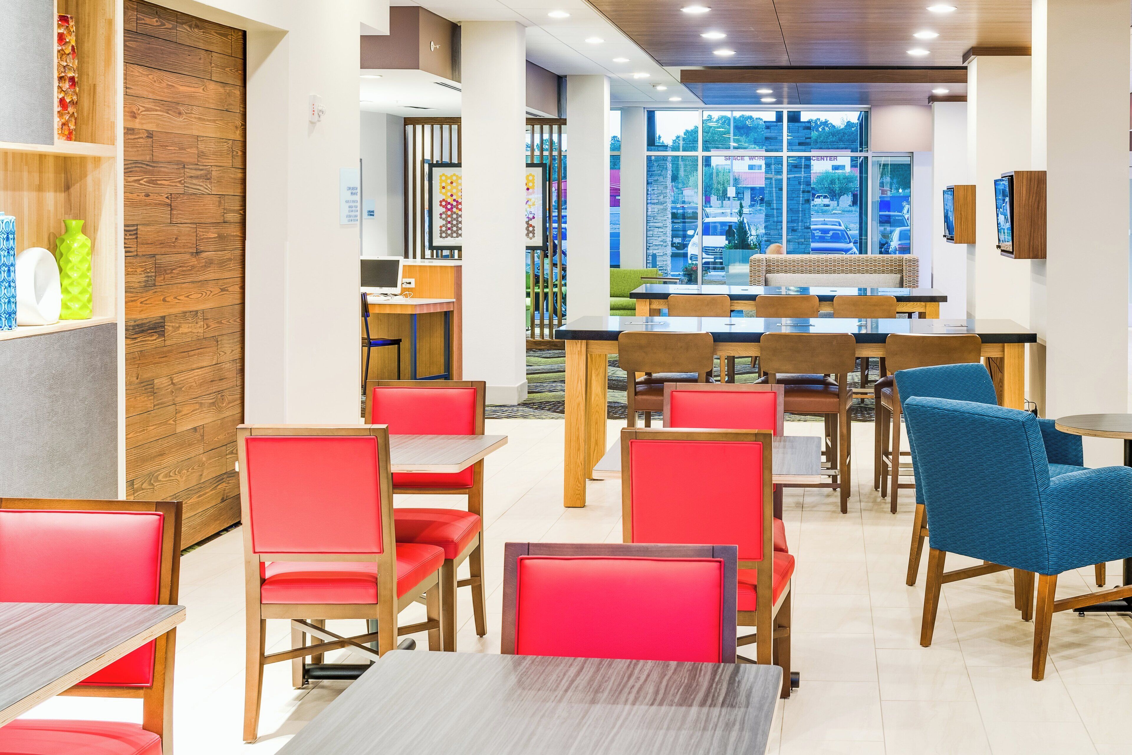 A restaurant interior with wooden panel walls, red and blue upholstered chairs, and a view of the street through large windows.