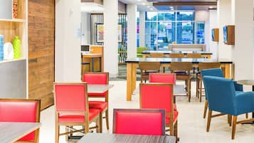 A restaurant interior with wooden panel walls, red and blue upholstered chairs, and a view of the street through large windows.
