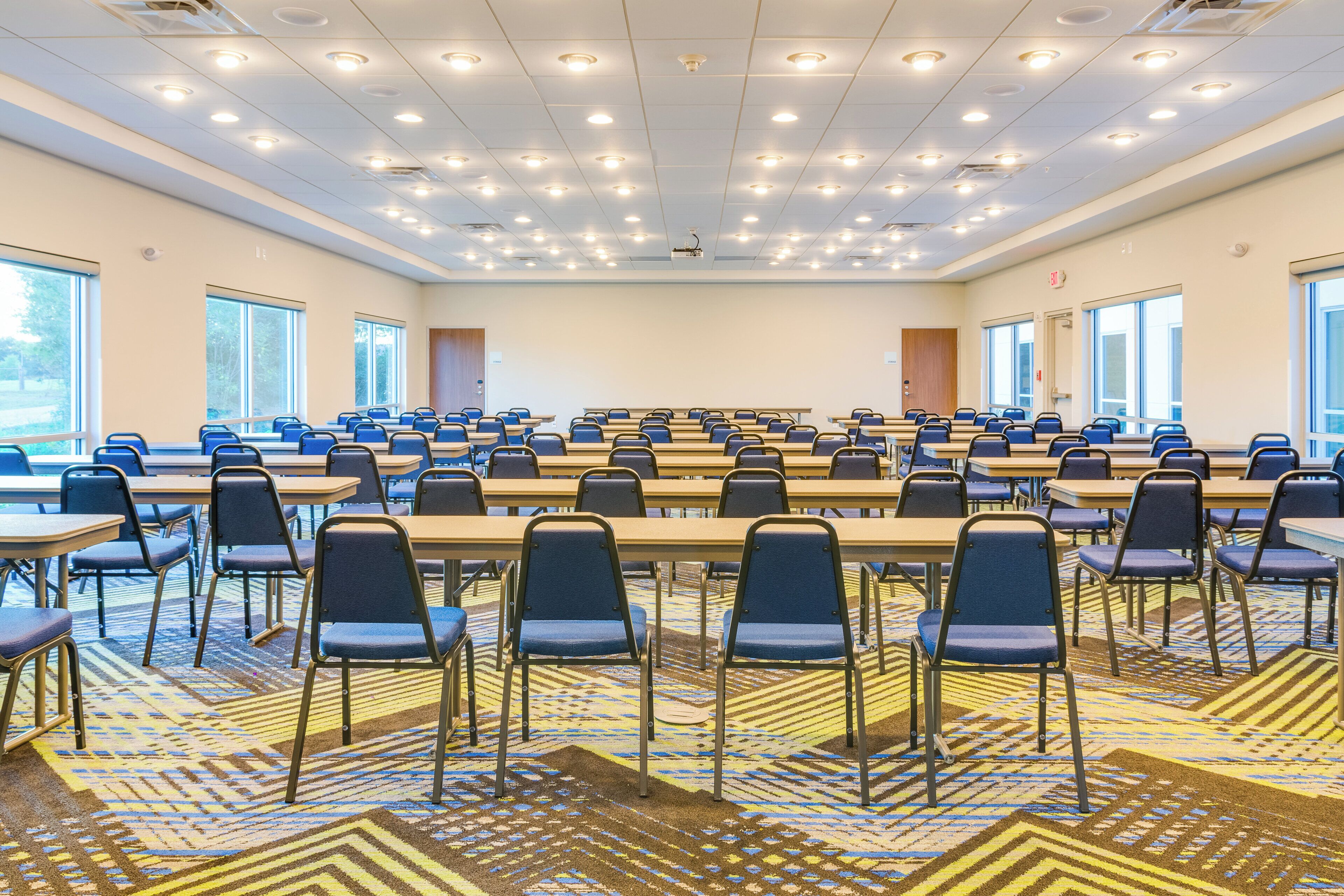 Ein Konferenzraum mit Tischen und Stühlen, großen Fenstern und einem gemusterten Teppich.