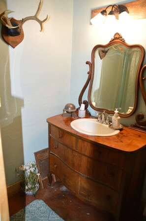 Ein Badezimmer mit einem Holzbadezimmermöbel, einem Waschbecken, einem Spiegel und einem aufgehängten Hirschkopf.