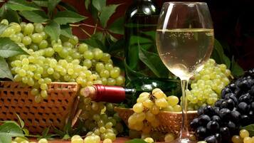 A table with a bottle of white wine, a glass of wine, and baskets of green and black grapes.