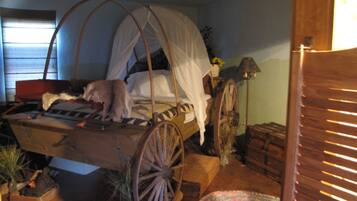 A rustic room with a bed featuring a canopy, a wooden cart-like structure, and a vintage lamp.