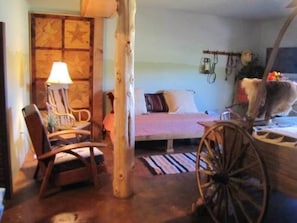 Una habitación rústica con una cama de madera, una silla, una lámpara y un carro de madera.