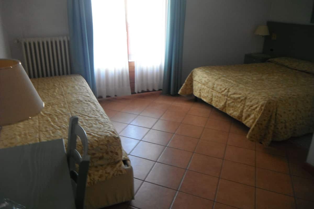 A hotel room with two beds, a chair, a lamp, and a radiator.