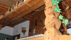 A wooden staircase with a carved design, a shelf with bottles, and a hanging plant. - Hotel Villa Rina (Bormio)