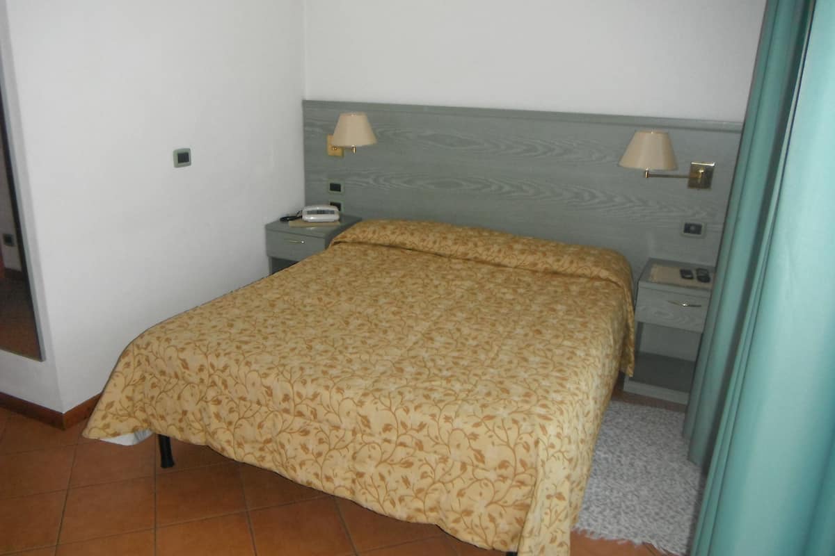 A bedroom with a bed, two bedside lamps, a nightstand with a phone, and a small table with a lamp.