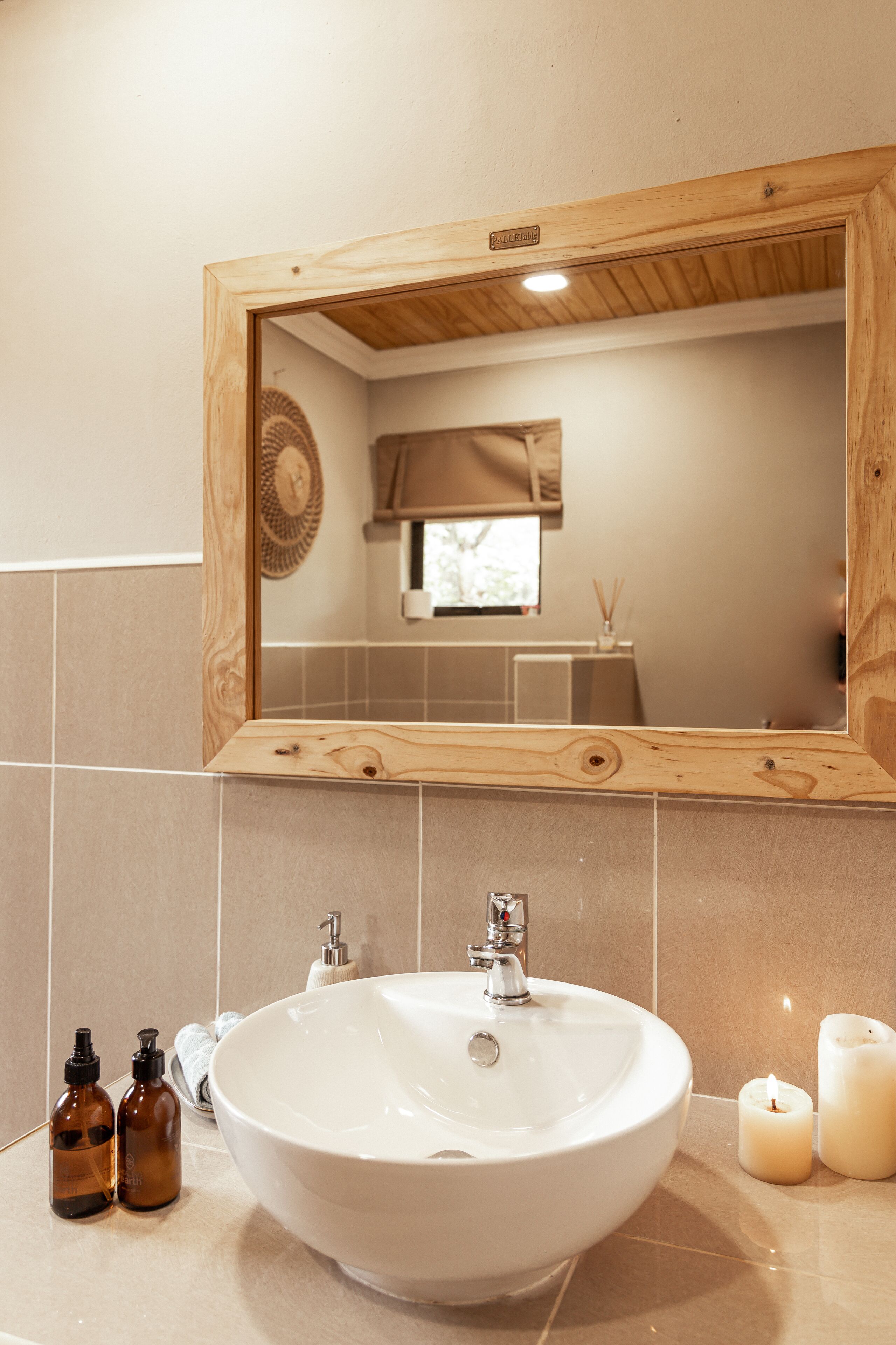 Een badkamer met een spiegel met houten rand, een witte wastafel en twee bruine flessen op het aanrecht.