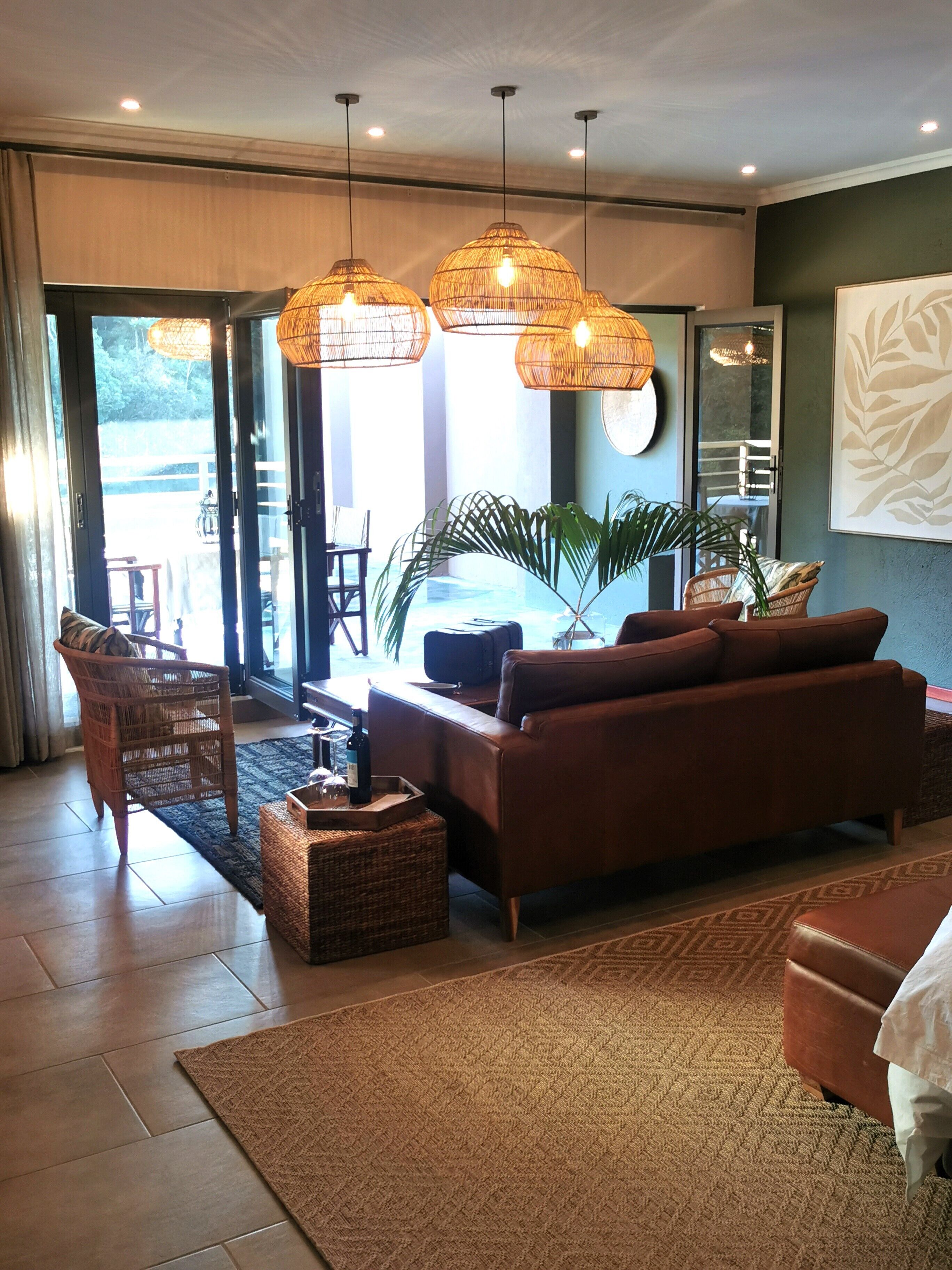 A modern living room with a brown leather sofa, wicker chairs, and a large window offering a view of the outdoors.