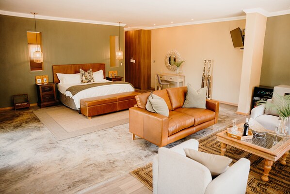 A modern hotel room with a large bed, a leather sofa, a desk, and a television.