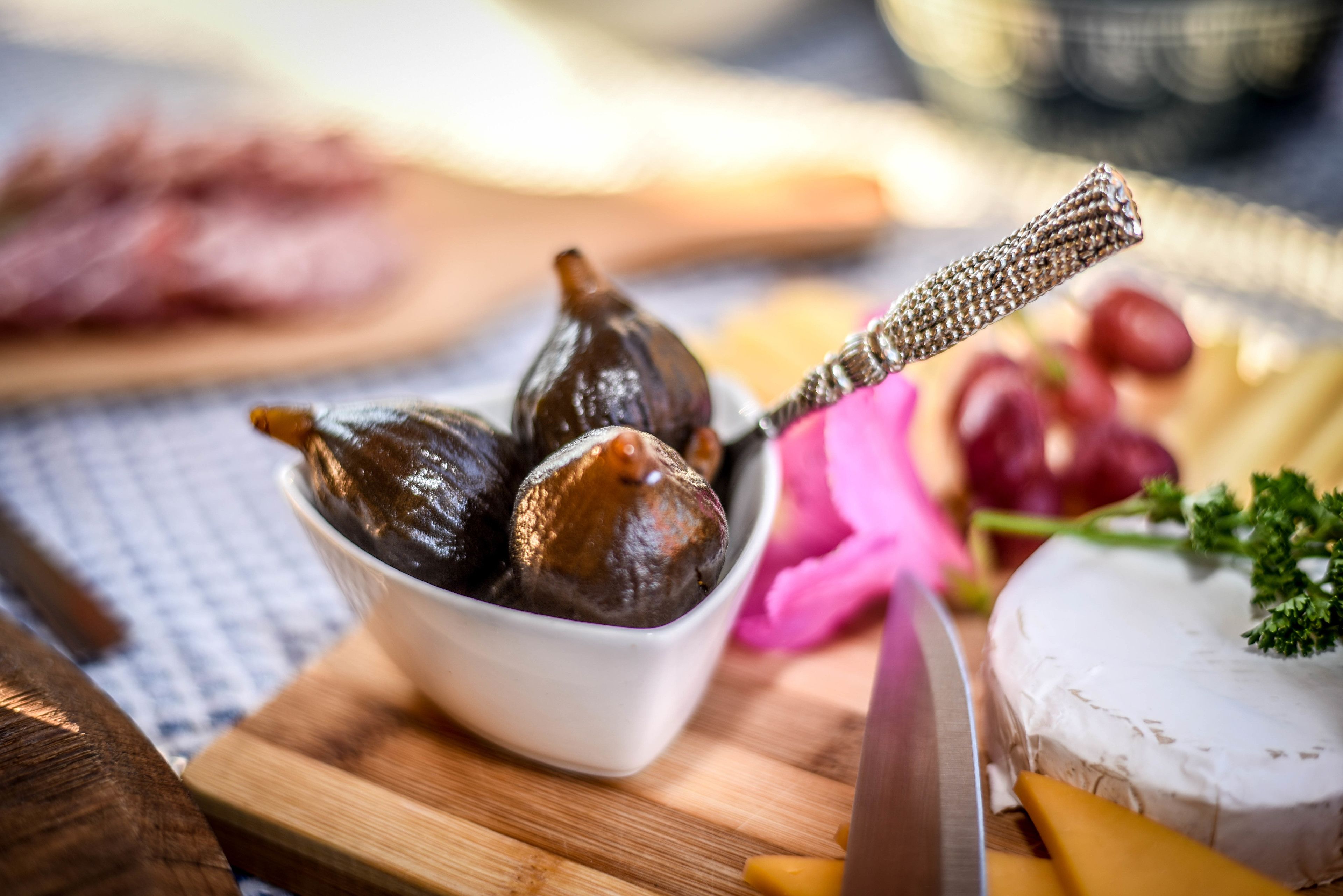 A wooden cutting board with a bowl of figs, a knife, and some cheese.