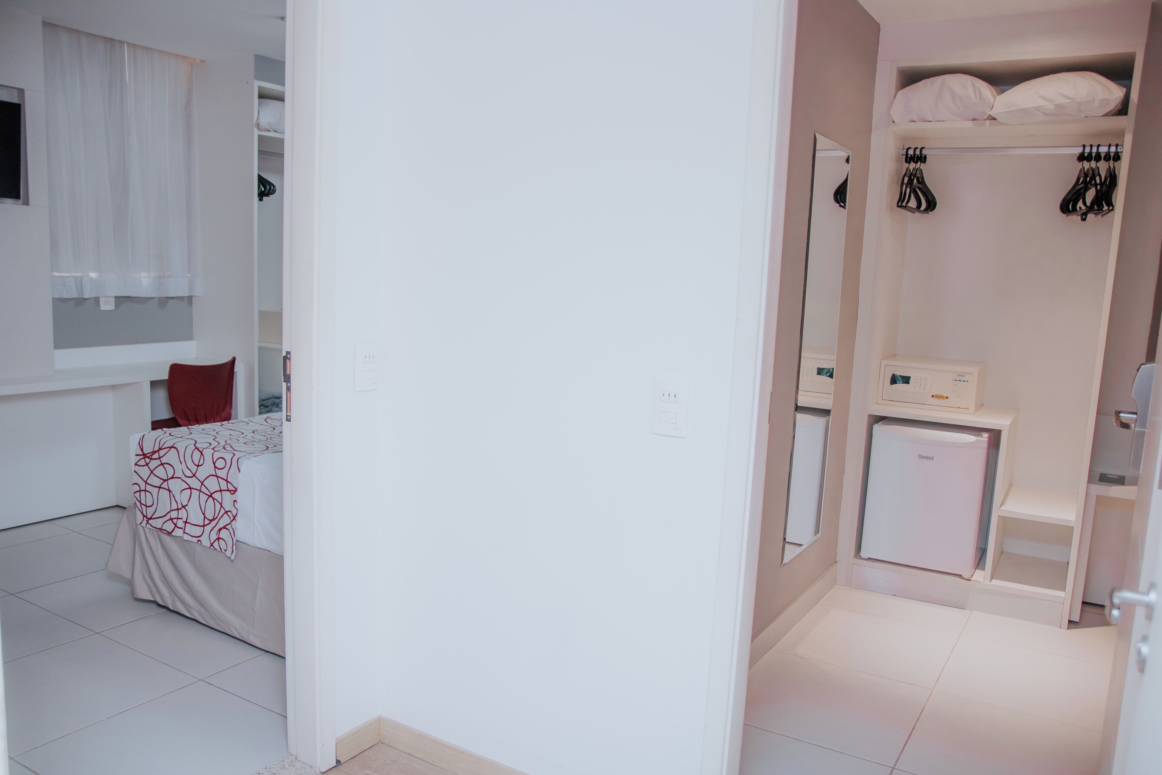 Een hotelkamer met een bed, een klein nachtkastje, een kledingkast, een spiegel en een minibar.