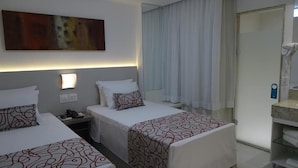 A hotel room with two beds, a large abstract painting on the wall, a bedside table with a lamp, and a bathroom with a shower and a toilet. - Rede Andrade Lapa (Rio de Janeiro)