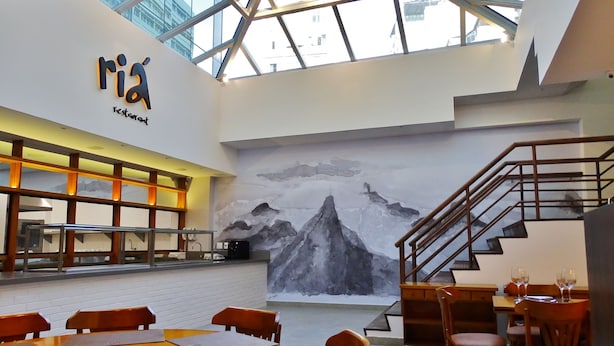 A modern restaurant interior with a high ceiling, a mountain mural, and a staircase. - Rede Andrade Lapa (Rio de Janeiro)