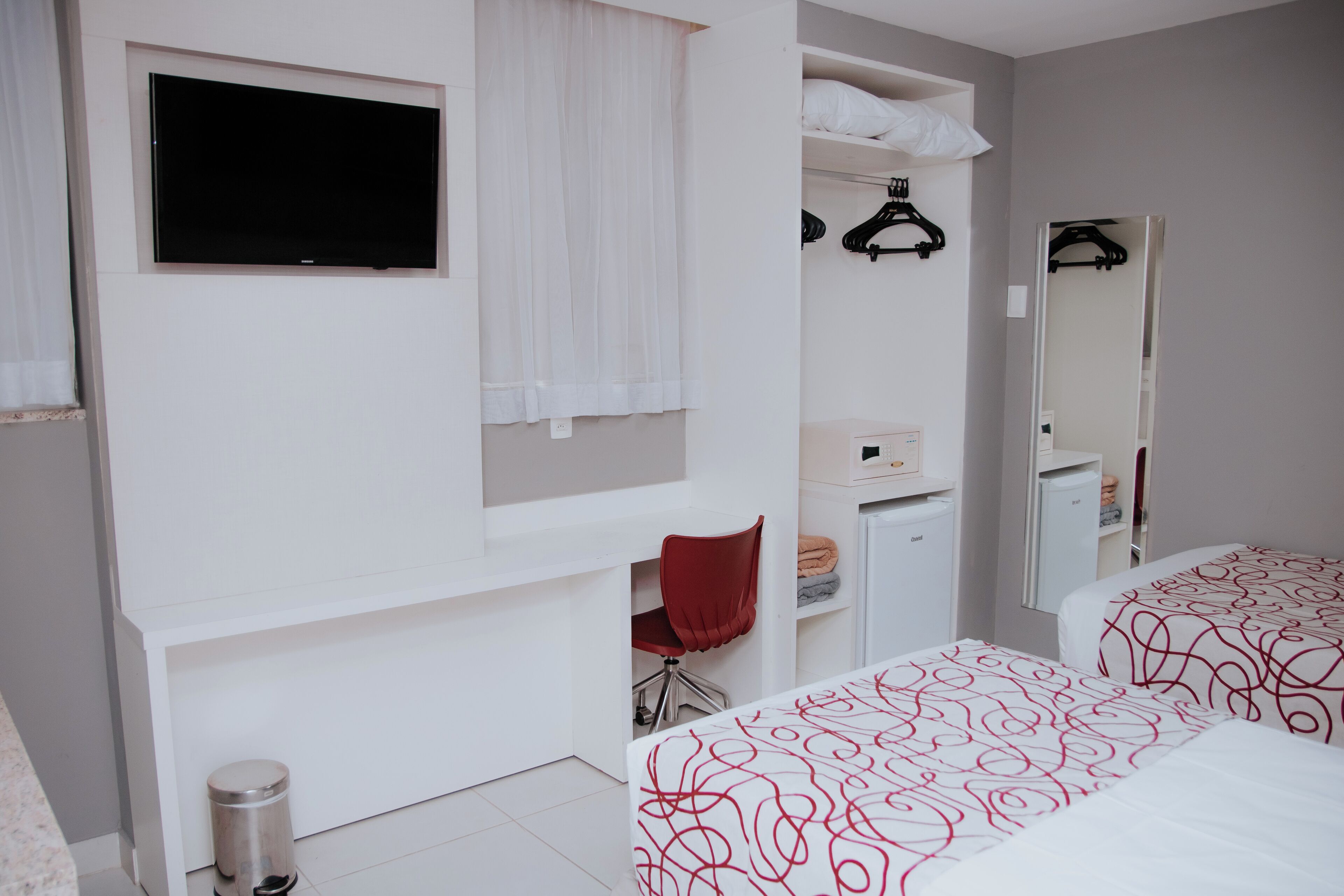 A hotel room with a bed, a desk, a chair, a TV, a wardrobe, and a mirror.