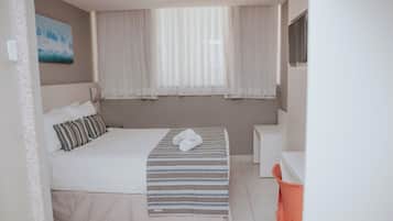 Une chambre d’hôtel bien rangée, avec un lit, une table de chevet et une fenêtre avec des rideaux.