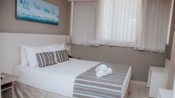 Una habitación de hotel con cama, mesita de noche, escritorio y ventana con cortinas.