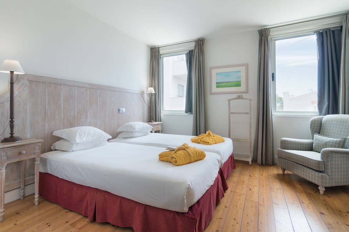 A hotel room with two beds, a desk, a chair, and a window with curtains.