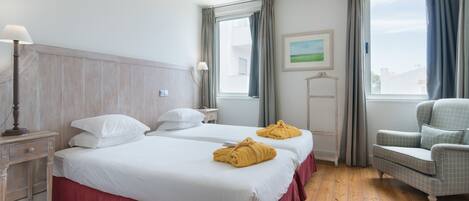 Habitación de hotel con dos camas, un escritorio, una silla y una ventana con cortinas.