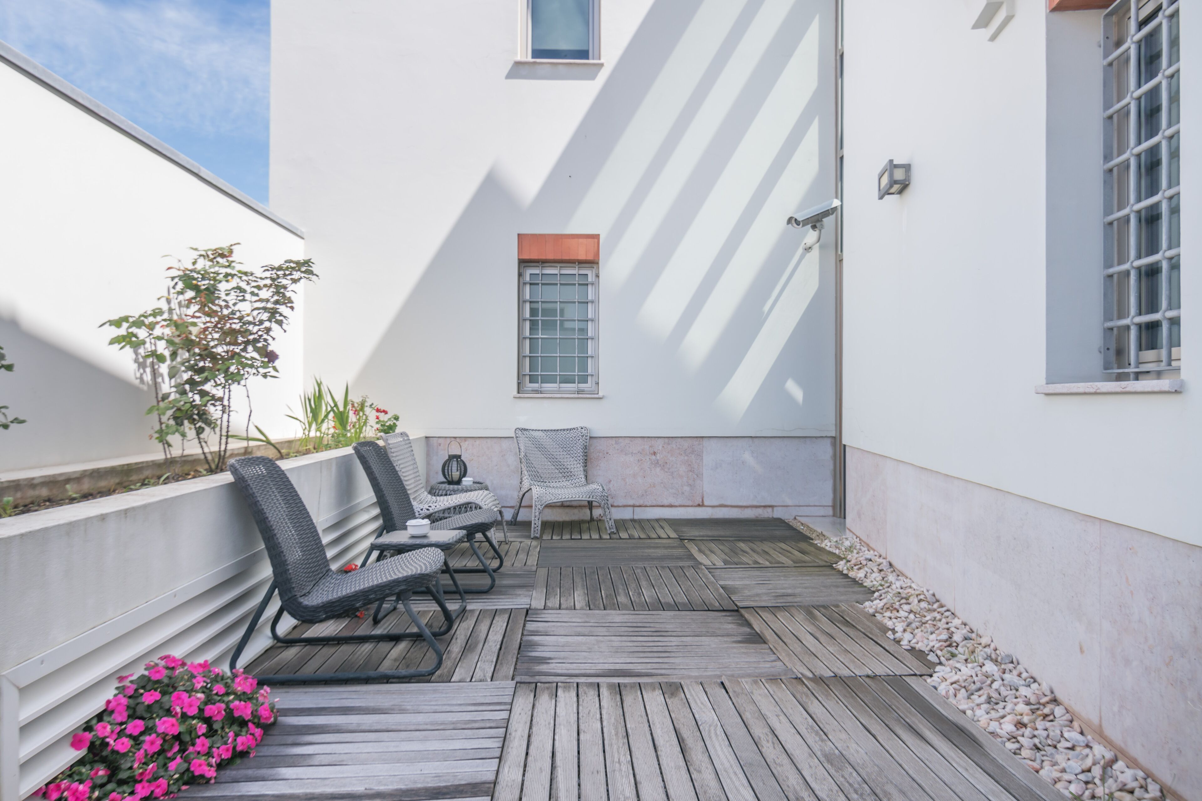 Een terras met rieten stoelen en een tafel, omringd door een houten terras en een witte muur.