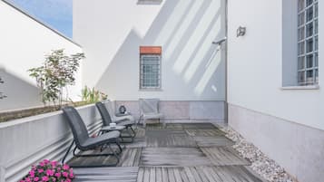 Een terras met rieten stoelen en een tafel, omringd door een houten terras en een witte muur.