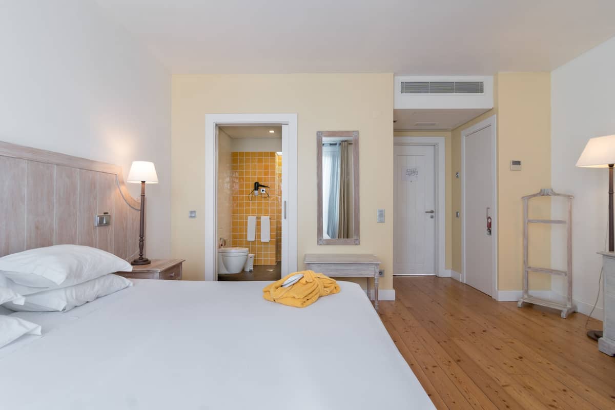A hotel room with a bed, bedside lamps, a bathroom with a yellow-tiled shower, and a wooden floor.