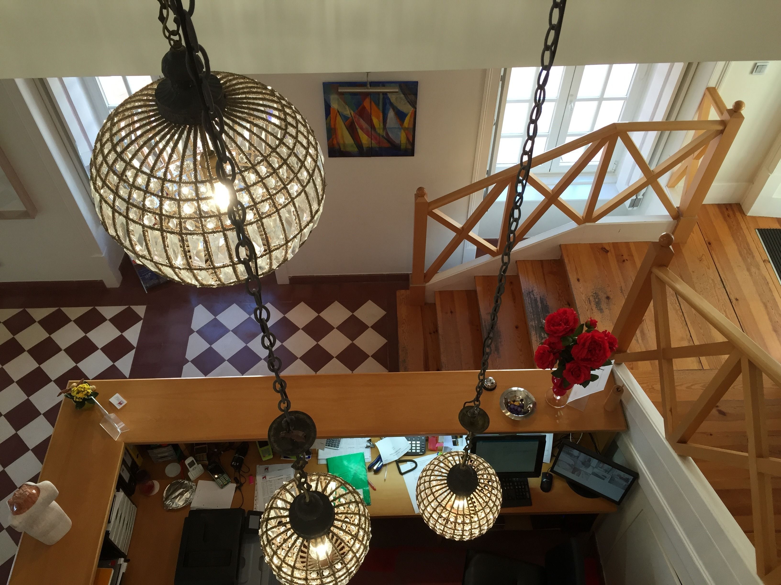 Um quarto com pé direito alto, escada de madeira, escrivaninha com computador e luminária pendente.