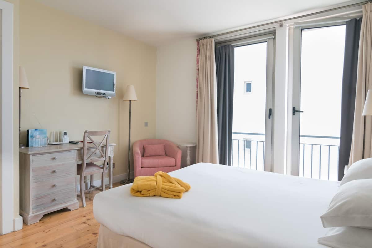 A hotel room with a bed, a desk, a chair, a TV, and a balcony.