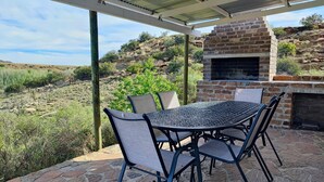Eine Terrasse im Freien mit einem Steintisch und -stühlen, einem Backstein-Barbecue und Blick auf eine hügelige Landschaft.