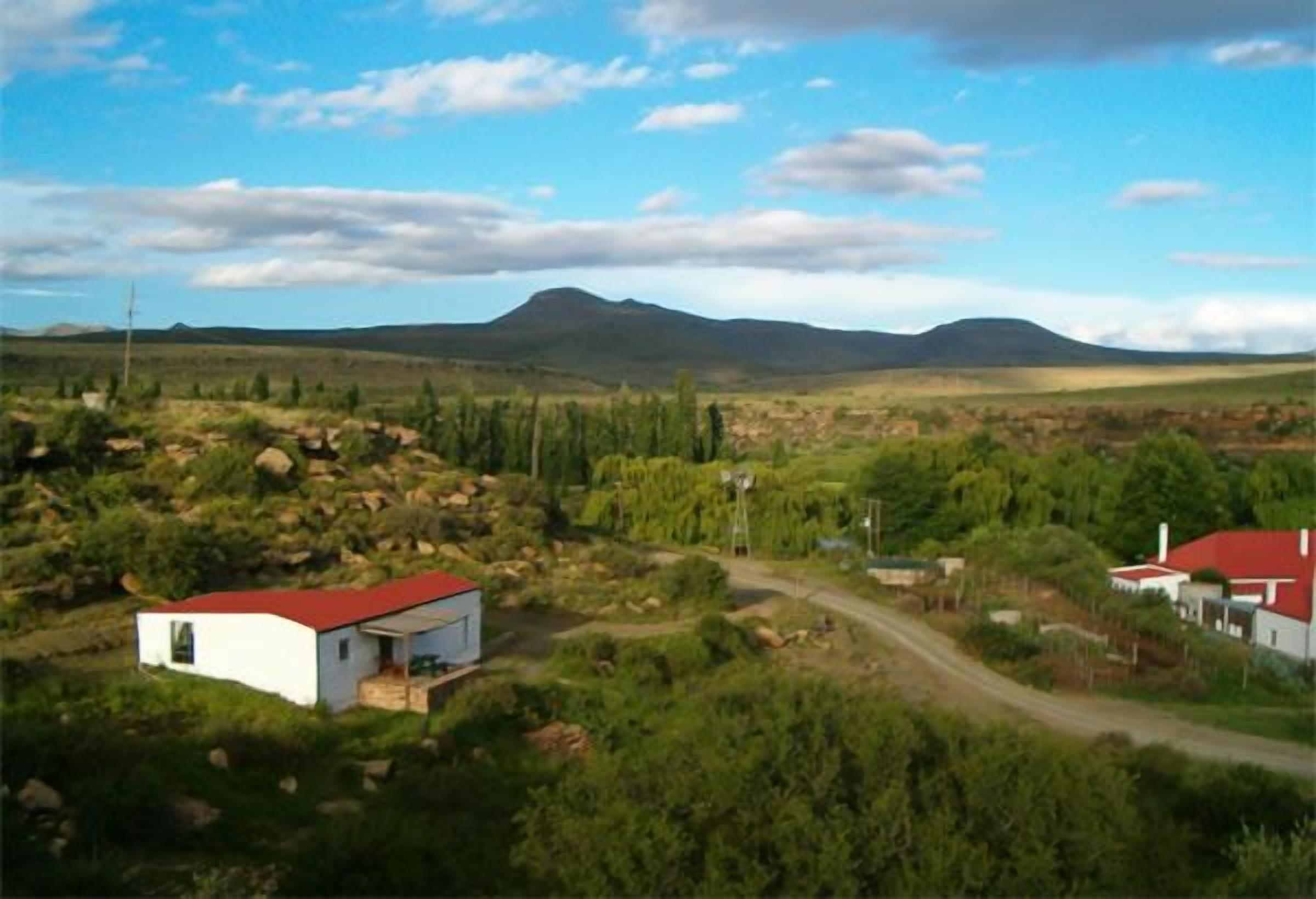 A rural landscape with a white building with a red roof, surrounded by greenery and a winding road.