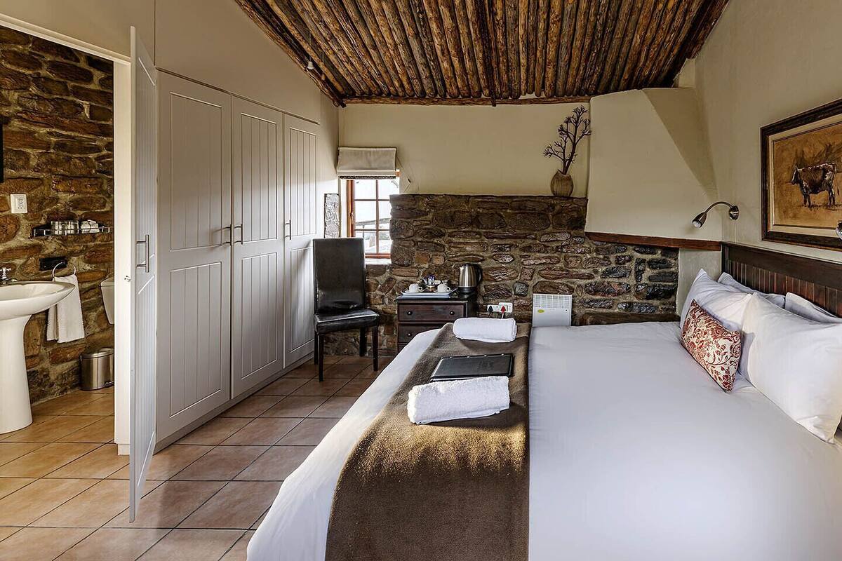 Une chambre avec un grand lit, un mur en pierre, un plafond en bois, un tableau et une petite table avec une lampe.