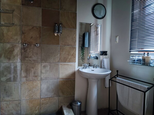 Une salle de bain avec un lavabo blanc, un miroir et une fenêtre avec des stores.