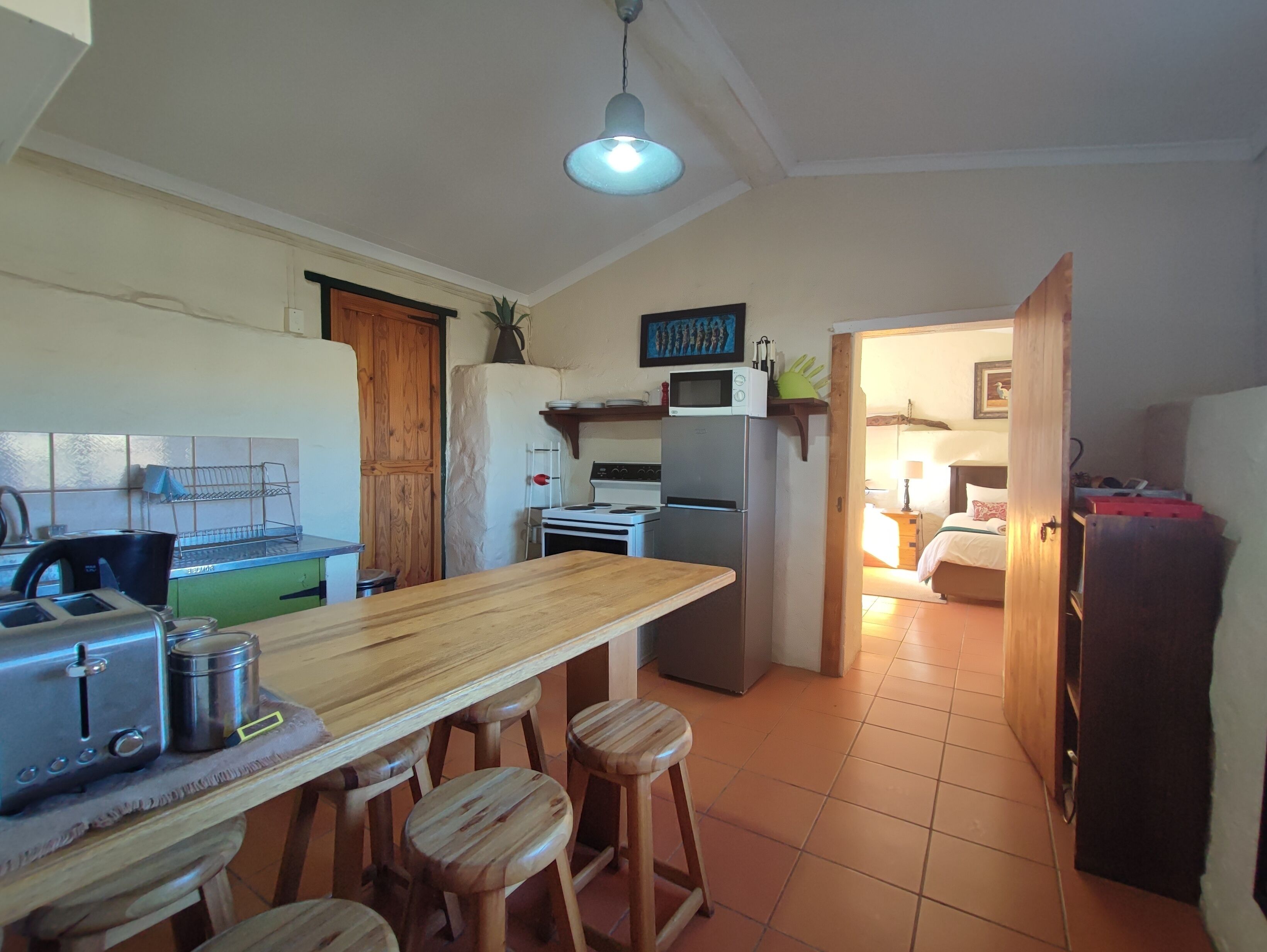 A compact kitchen with a wooden table, stools, a refrigerator, a microwave, and a stove.
