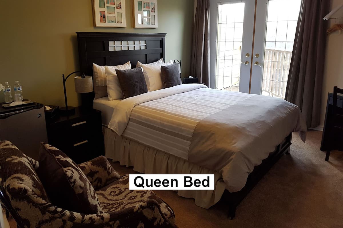Habitación de hotel con una cama grande, una mesita de noche, una silla y una ventana con cortinas.