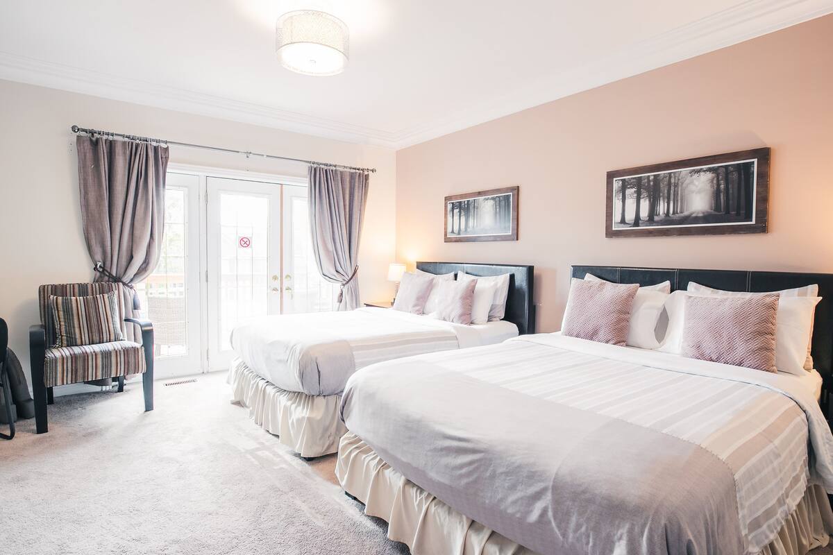 Habitación de hotel con dos camas, una silla, una puerta con cortinas y un cuadro en la pared.