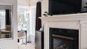 A modern living room with a fireplace, a flat-screen TV, and a dining area visible through a glass door.
