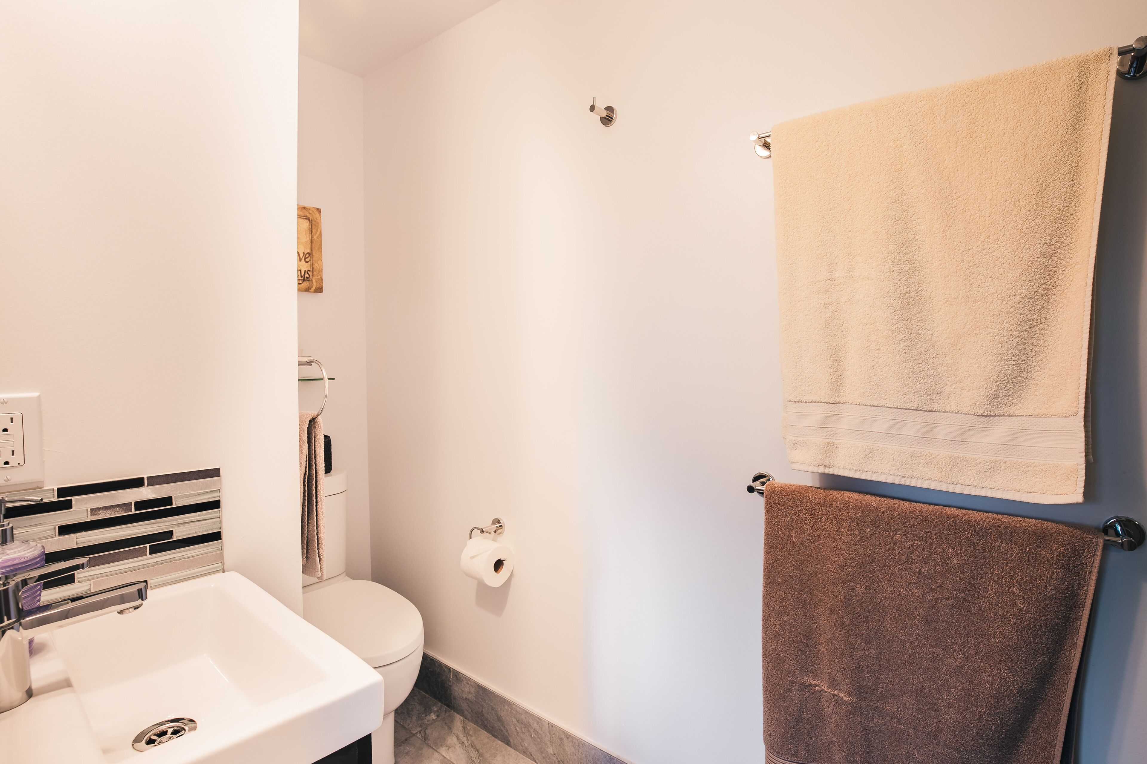 A bathroom with a white sink, toilet, and towel rack with two towels.