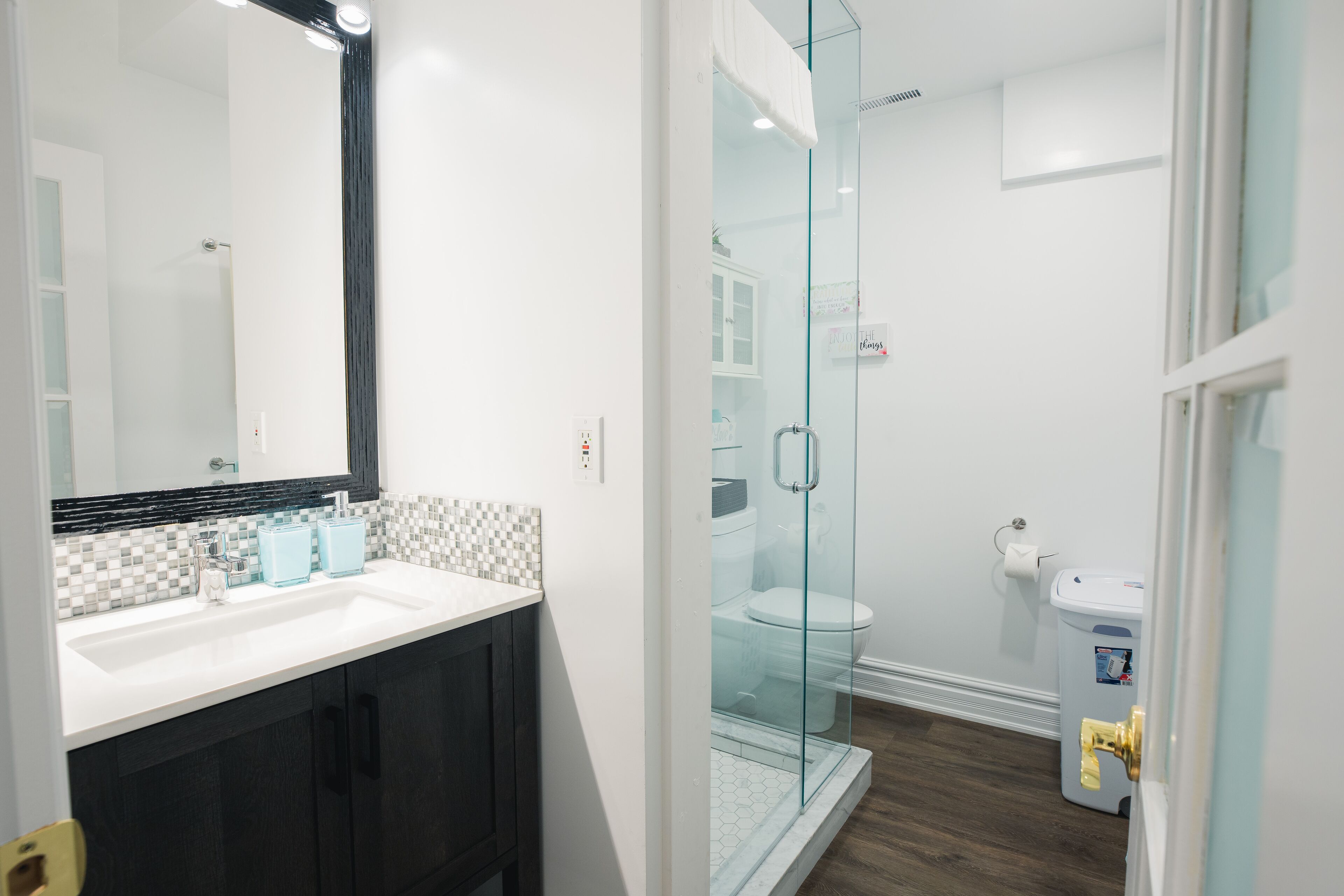 A modern bathroom with a glass-enclosed shower, a white sink with a black countertop, and dark wooden cabinets.