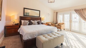 A spacious bedroom with a large bed, a nightstand, a chair, and a window with curtains.