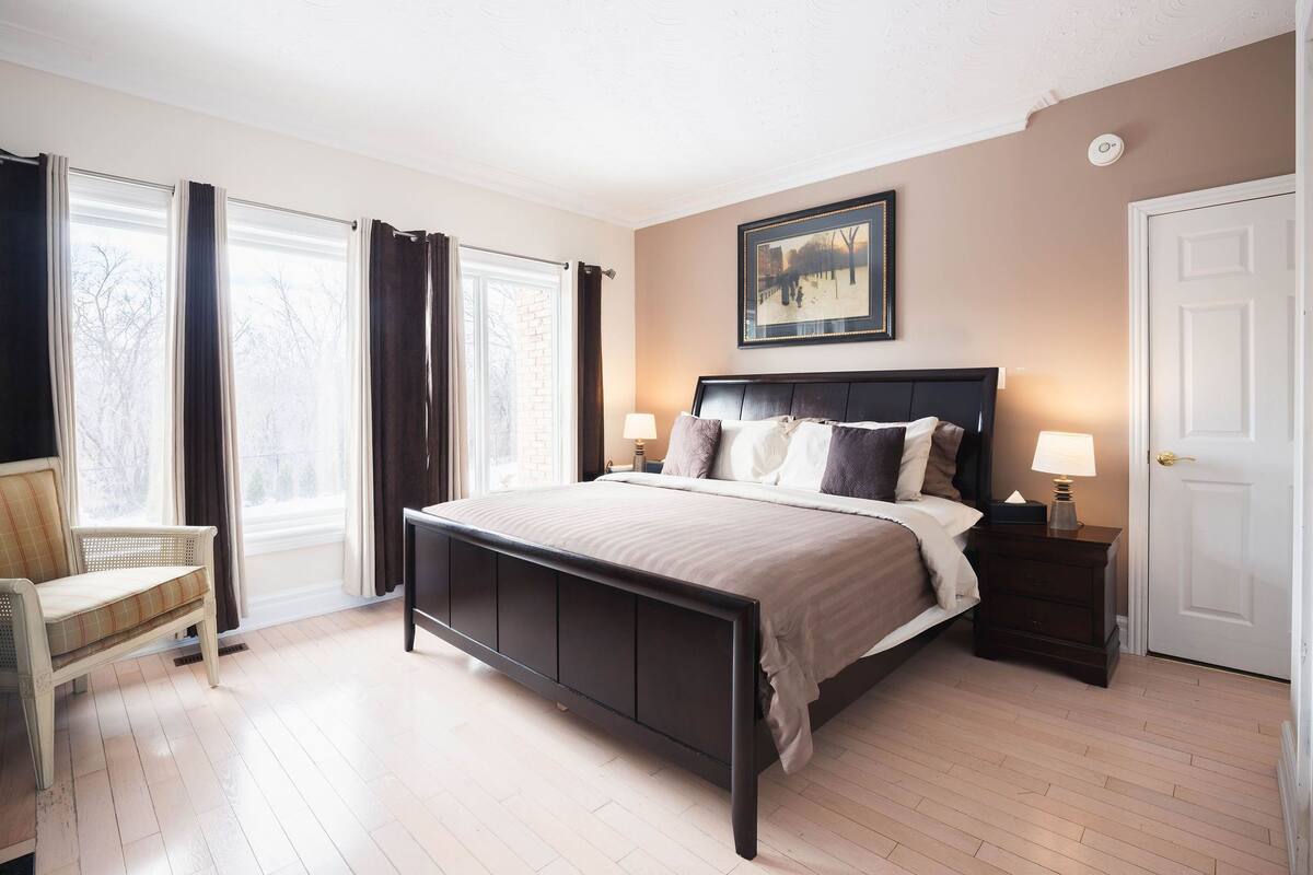 Un dormitorio con cama, mesitas de noche, una silla y una ventana con cortinas.