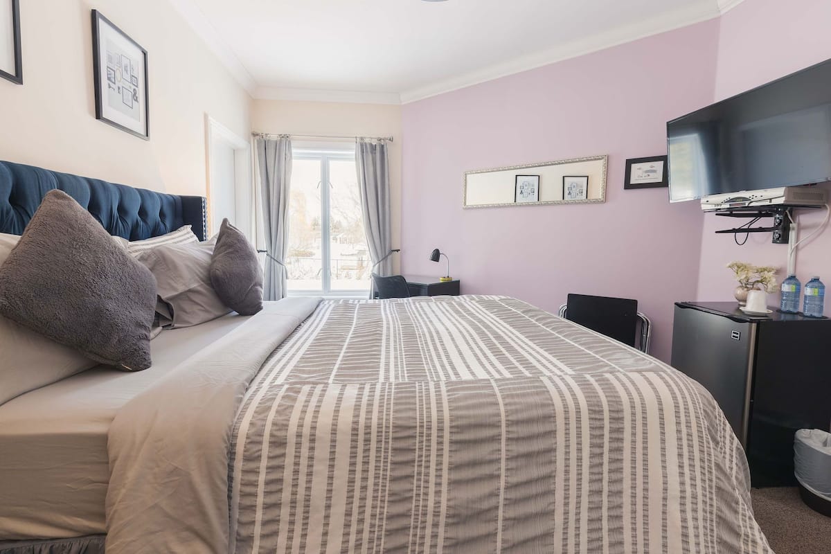 Habitación de hotel con una cama grande, un escritorio con computadora, un televisor y una ventana con cortinas.