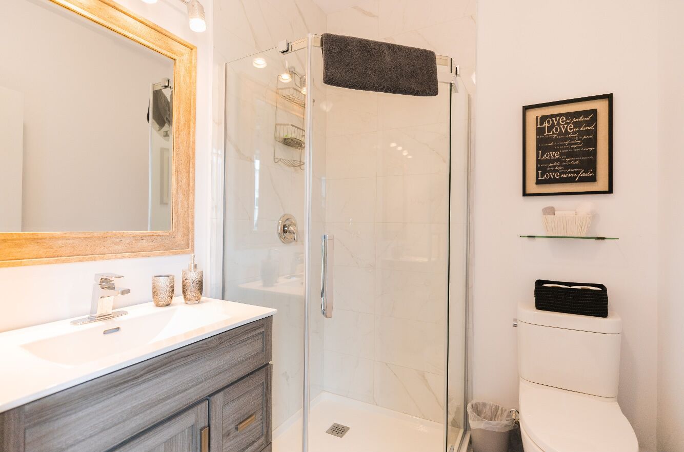 Un baño moderno con ducha de vidrio, un espejo grande, un lavamanos blanco y una cita enmarcada en la pared.