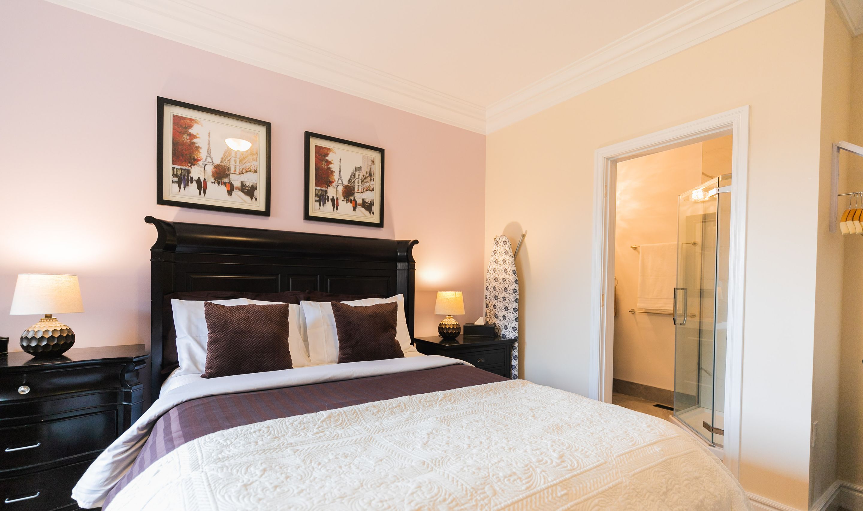 A queen bed with a white quilt, dark headboard, and two framed pictures on the wall.