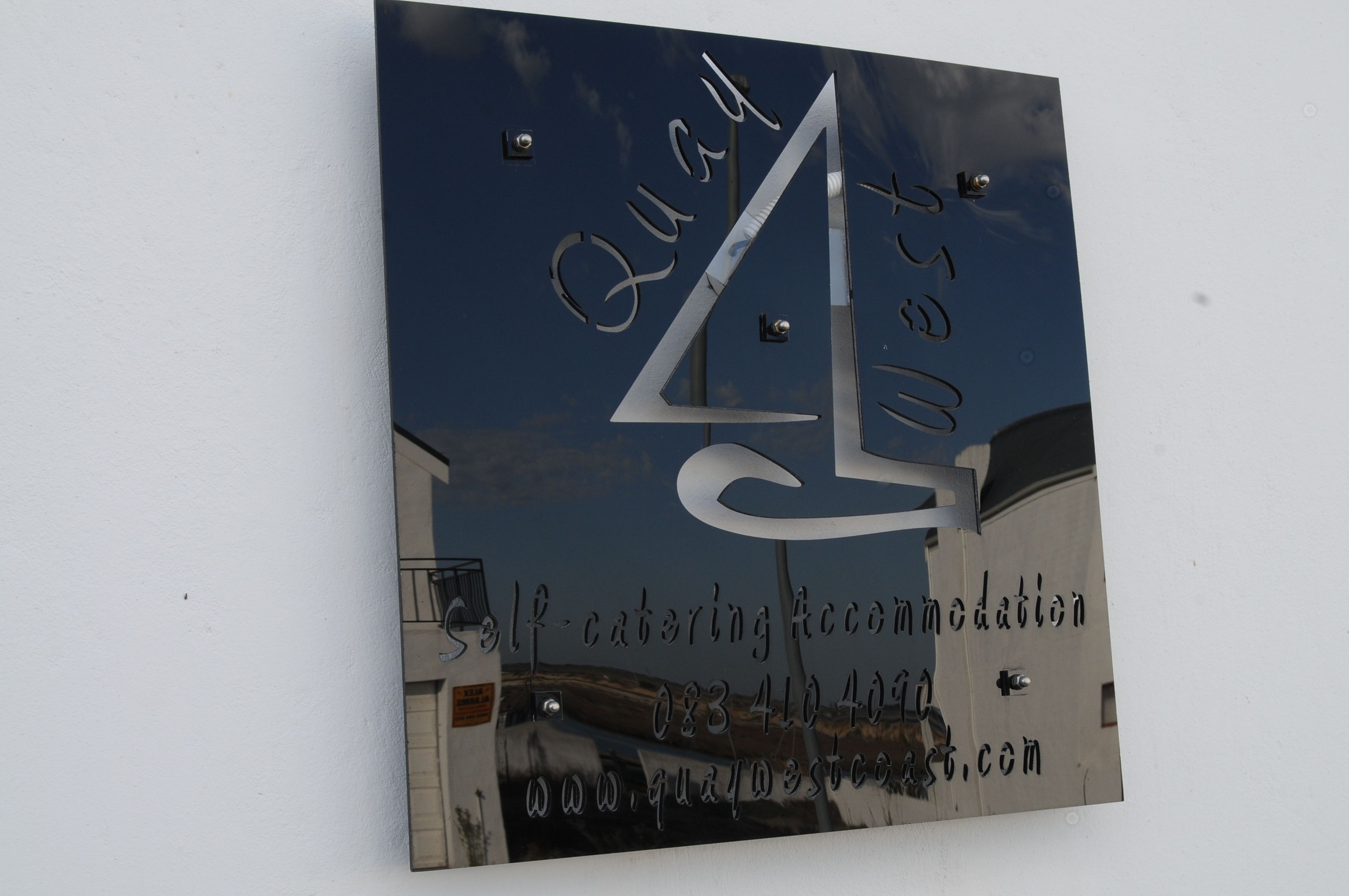 A sign with the name "Quay West" and contact information for self-catering accommodation.