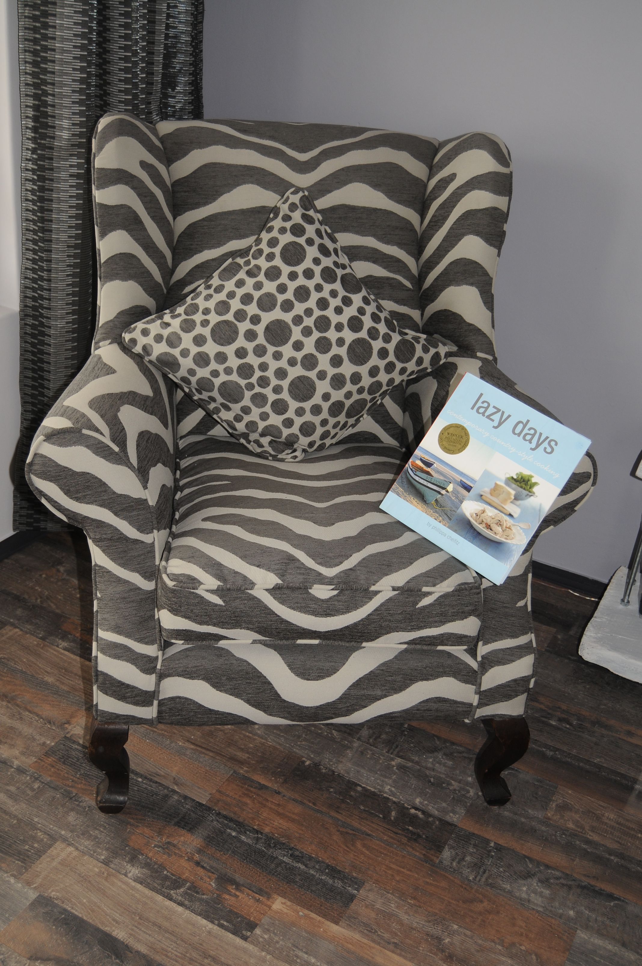 Un sillón estampado con diseño de cebra, con un cojín de lunares y un libro titulado 'lazy days'.