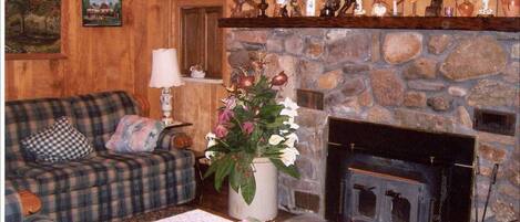 A cozy living room with a plaid sofa, a fireplace, and various decorative items on shelves above the fireplace.